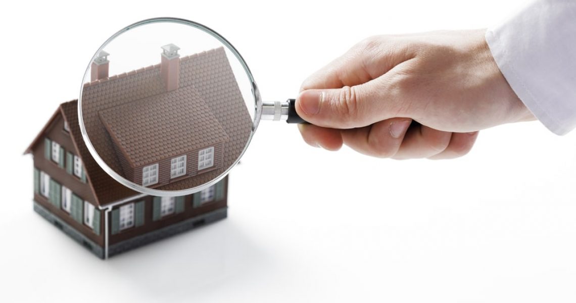 Hand holding magnifying glass over a house